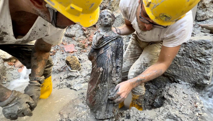 Due esperti scavano una statuetta di bronzo