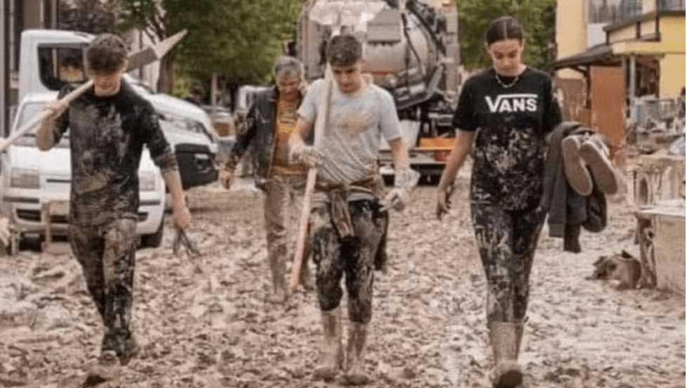 Tre giovani coperti di fango che aiutano a pulire le strade del paese allagato.